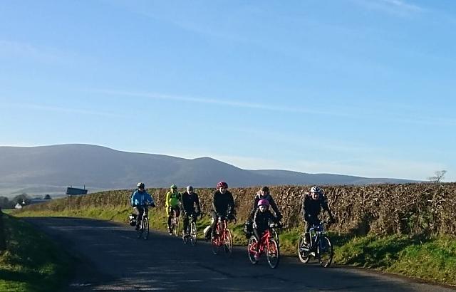Cyclists on road enjoying the sunshine, with Criffel in the background.