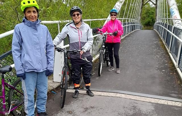 photo of 3 women standing with their bikes next to a bridge
