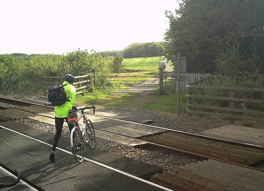 A cyclist pushes their bicycle across a level crossing