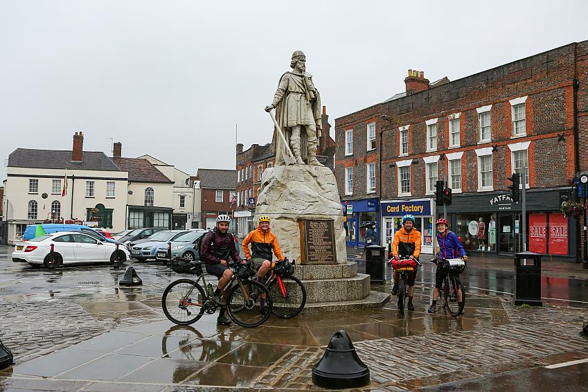 Four cyclists stand by the King Alfred memorial in Wantage. It's raining. No one else is about
