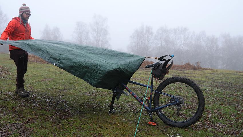 A man spreads his tarp over his bike before pegging it down