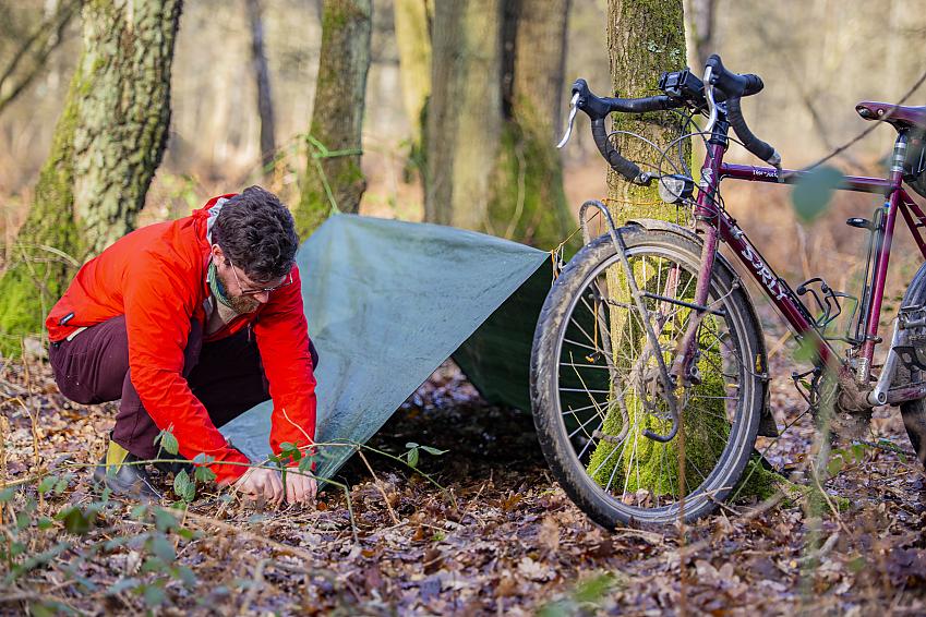 A man setting up a simple A-frame tarp between two trees