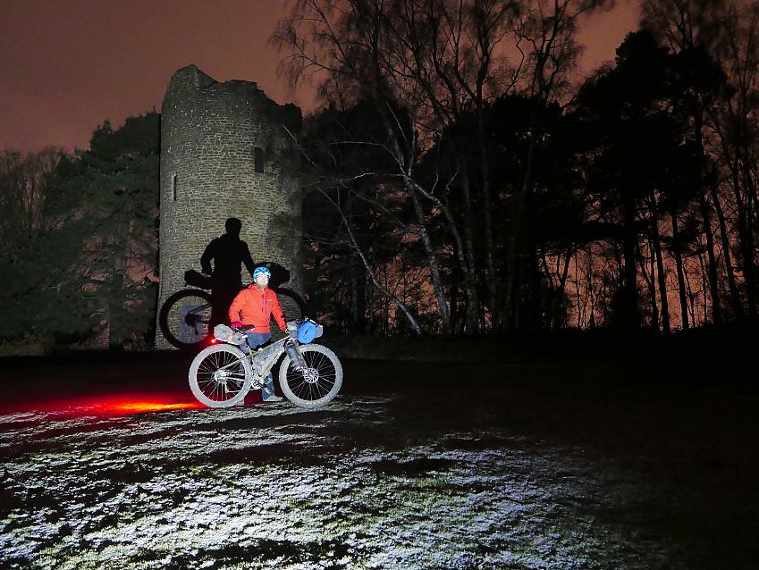 Cyclist stands in front of a folly at night