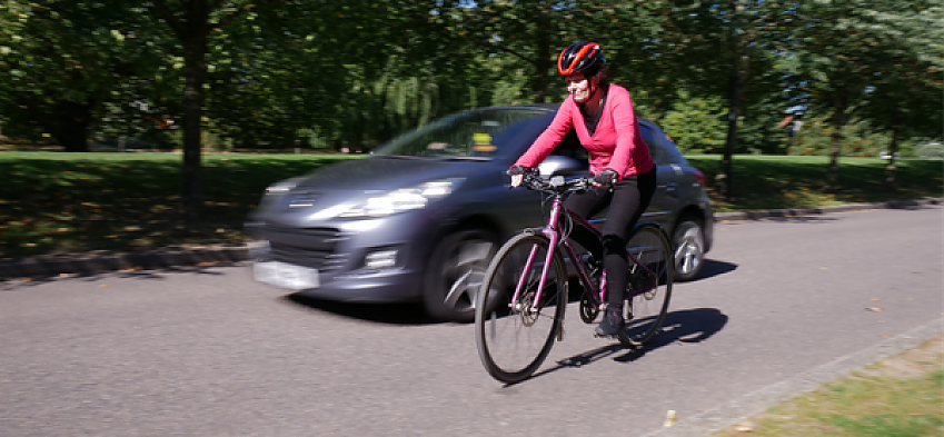 A woman is cycling along a road as a car overtakes her
