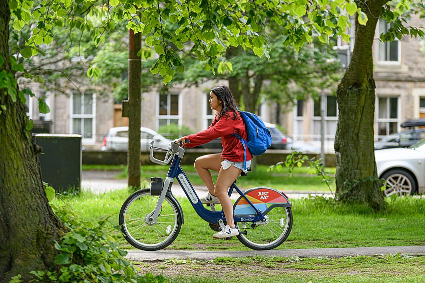A young woman riding a hire bike through the Meadows in Edinburgh