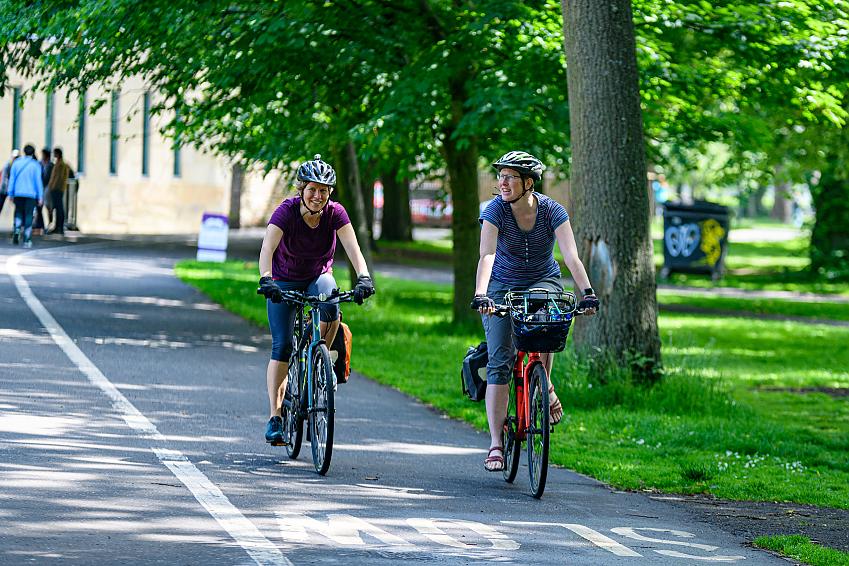 Two women smiling as they cycle through the Meadows in Edinburgh