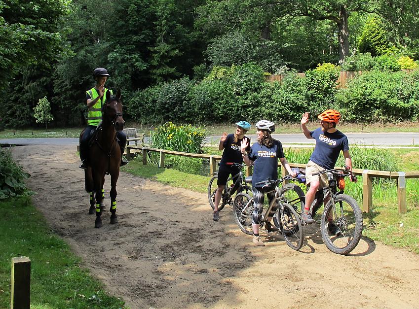A horse rider smiles and waves at three cyclists who have moved over to the side of the path to let him pass