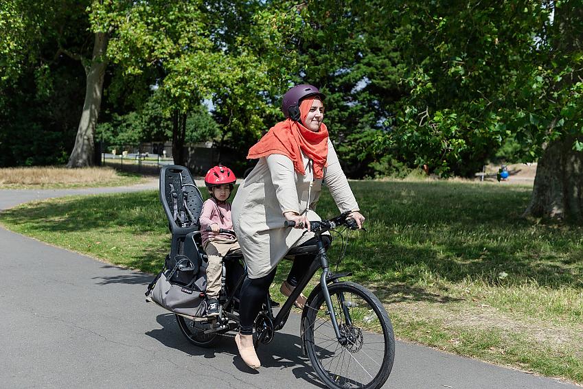 Woman cycling through park with child in seat behind her