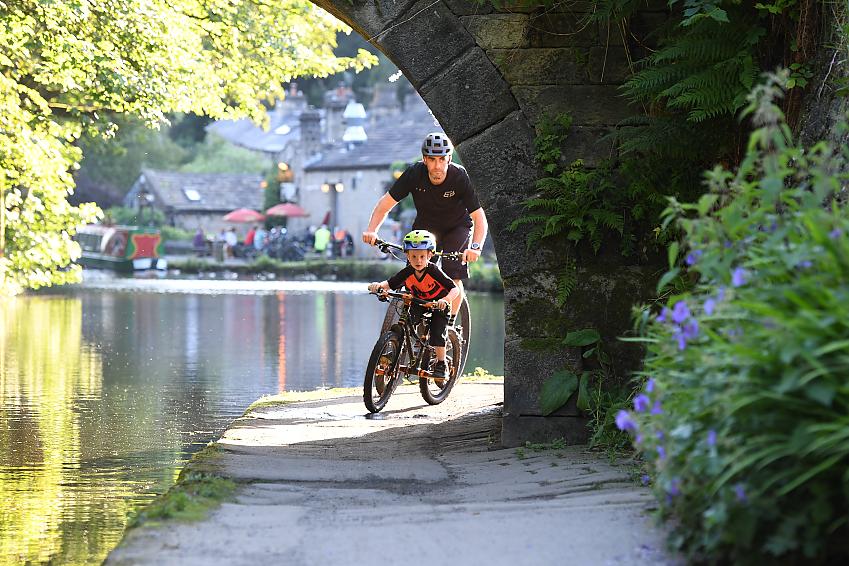 A man and young boy cycle under a bridge on a canal towpath