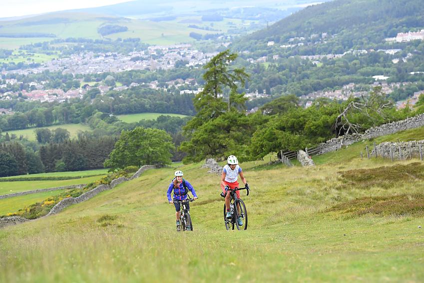 Two women riding up a grassy hill on mountain bikes