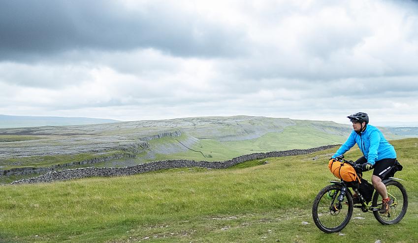 Mountain biker riding past a dramatic rocky outcrop in green countryside