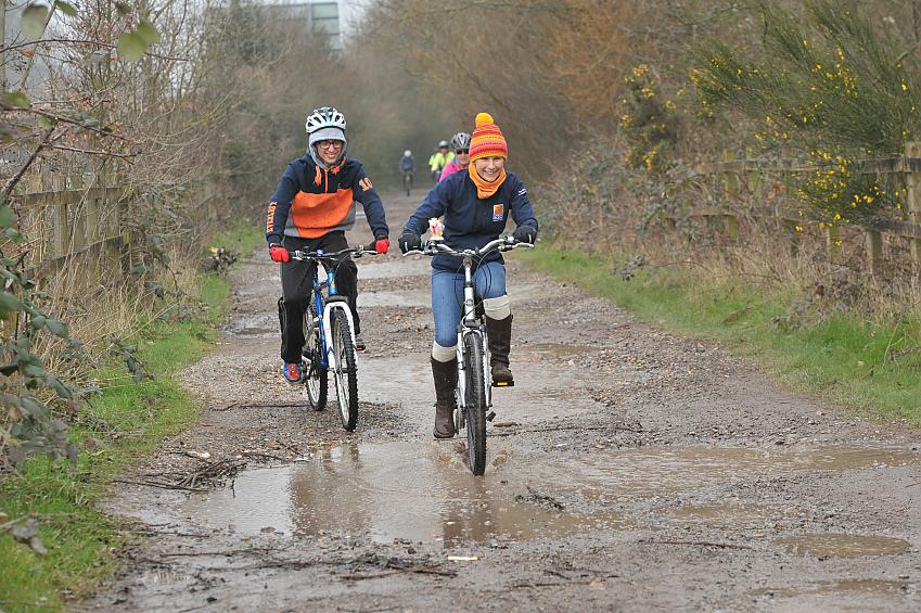 People laugh as they ride through puddles on a muddy track