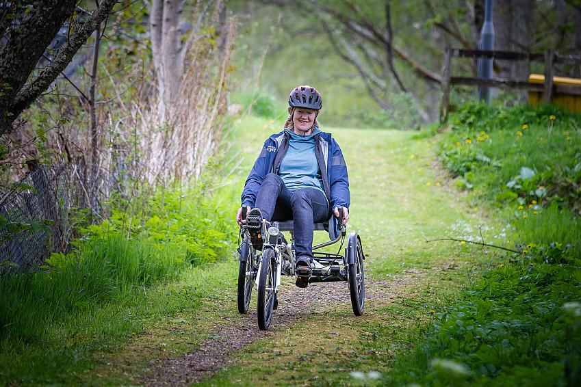 Woman riding a recumbent tricycle along a woodland path