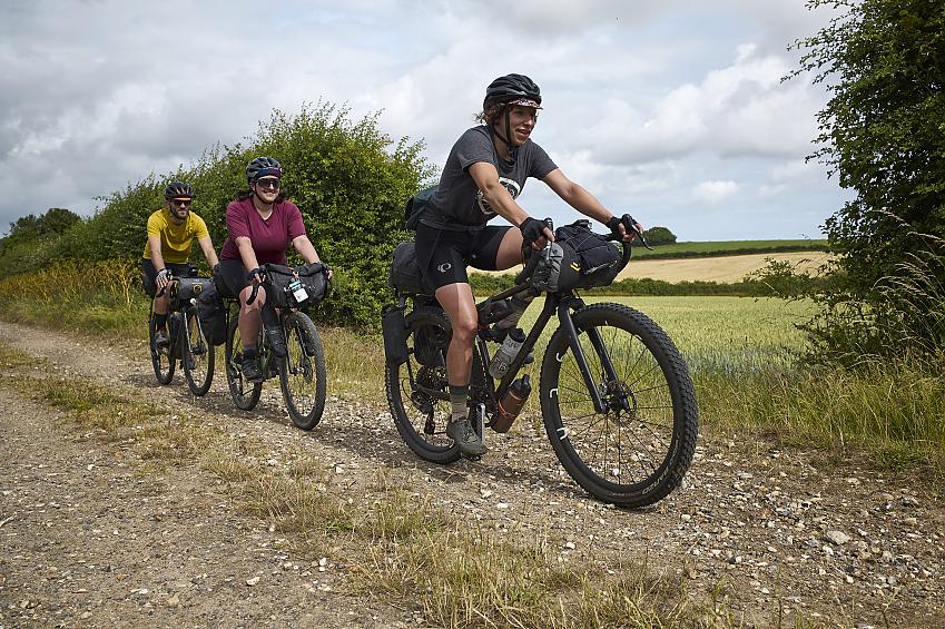 Three people cycle along a gravel track through the countryside