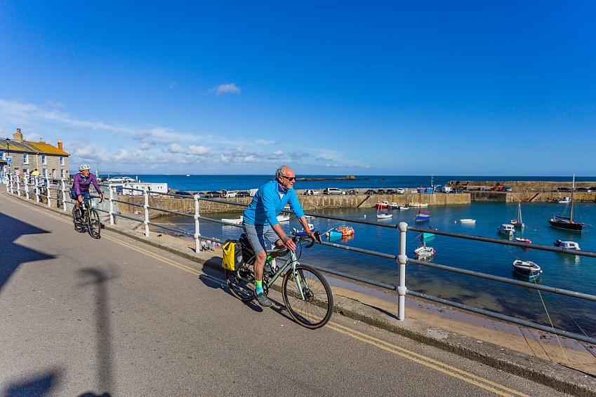 Two people cycle along the side of a harbour