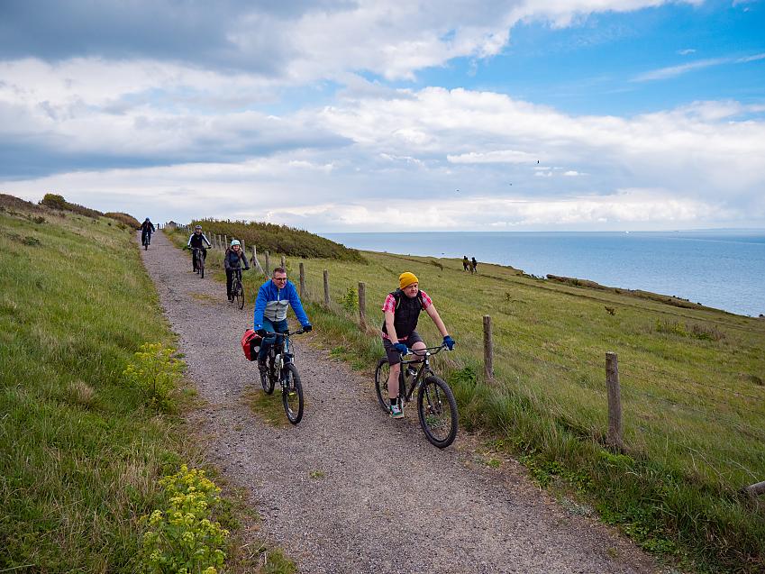 People cycle along a gravel coastal path high above the sea