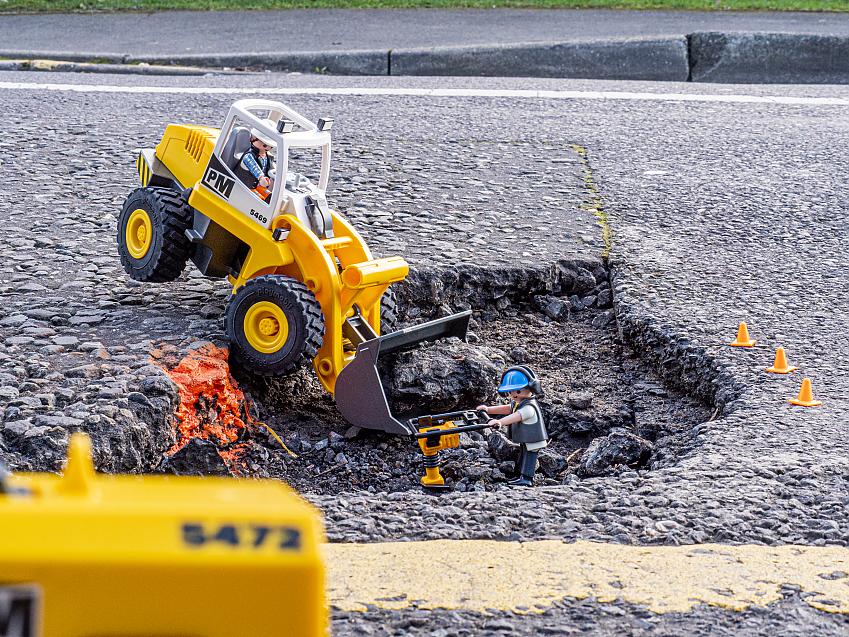 A toy digger and person figure fixing a giant-looking pothole