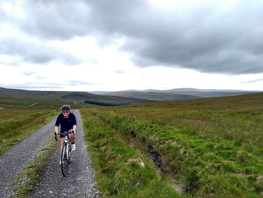 A woman cycles along a gravel track across rolling moorland