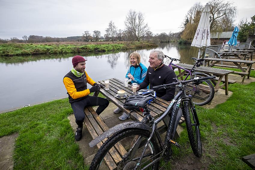 People sat at a table in a pub garden by a river with bikes