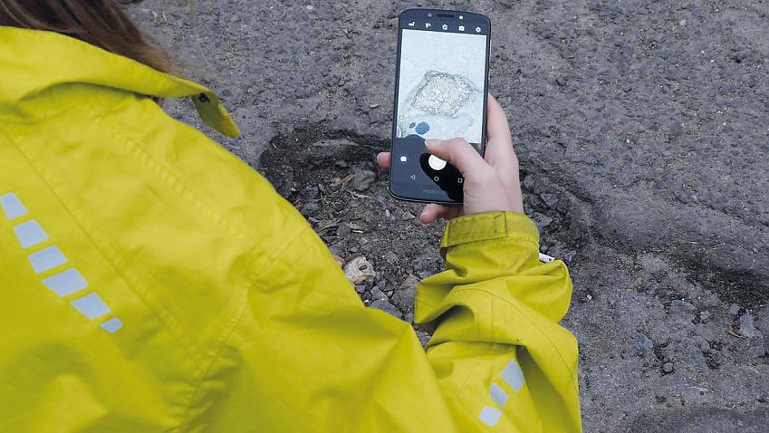 Close-up of person taking a photo of a large pothole with their phone