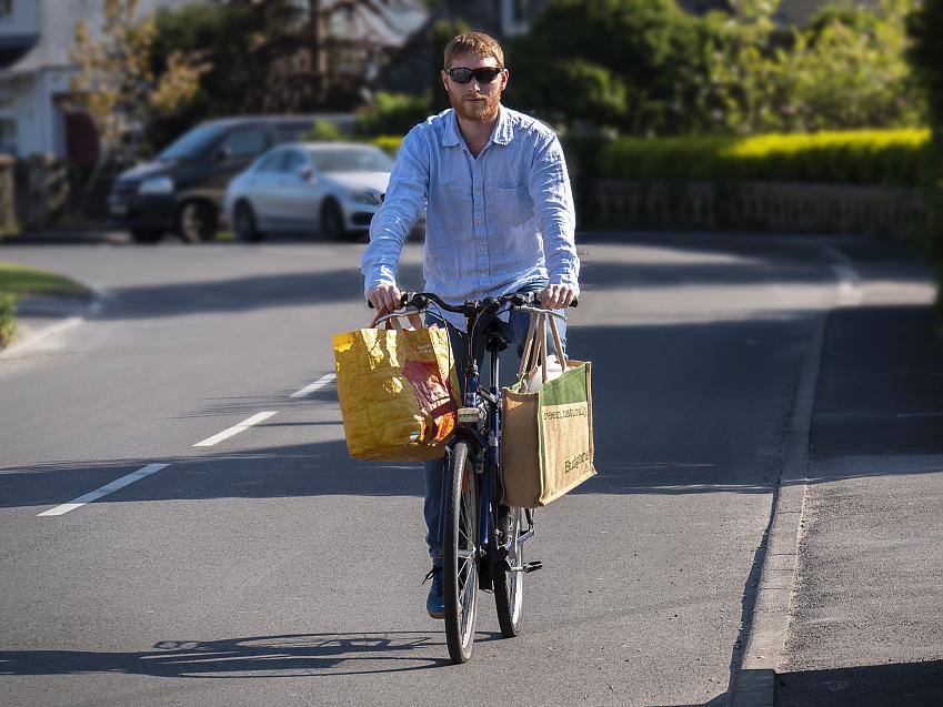 A man cycling with two shopping bags hanging from his handlebars