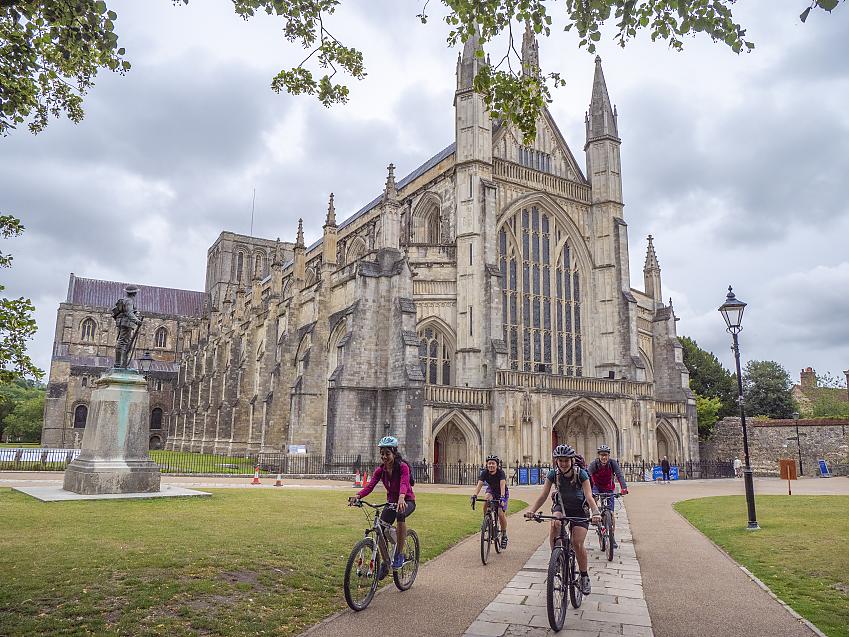 Four people cycle past Winchester Cathedral, one of the largest cathedrals in Europe