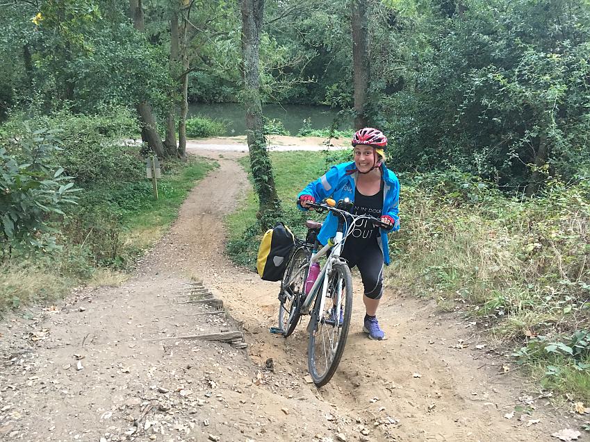 A cyclist wheeling her bike up a trail with a full pannier
