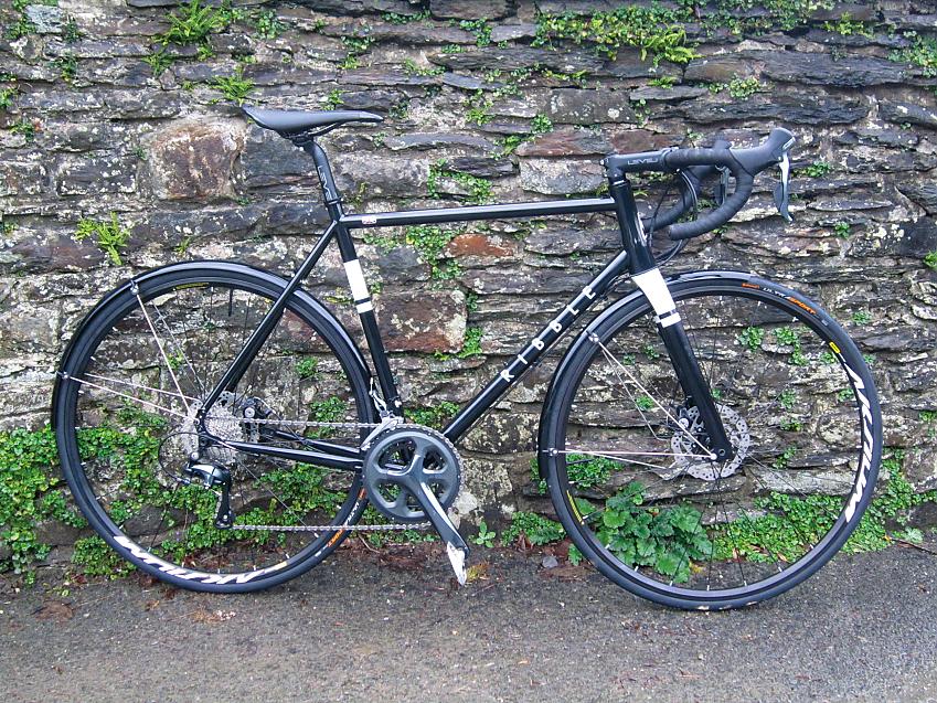 A black and white road bike leaning against a stone wall