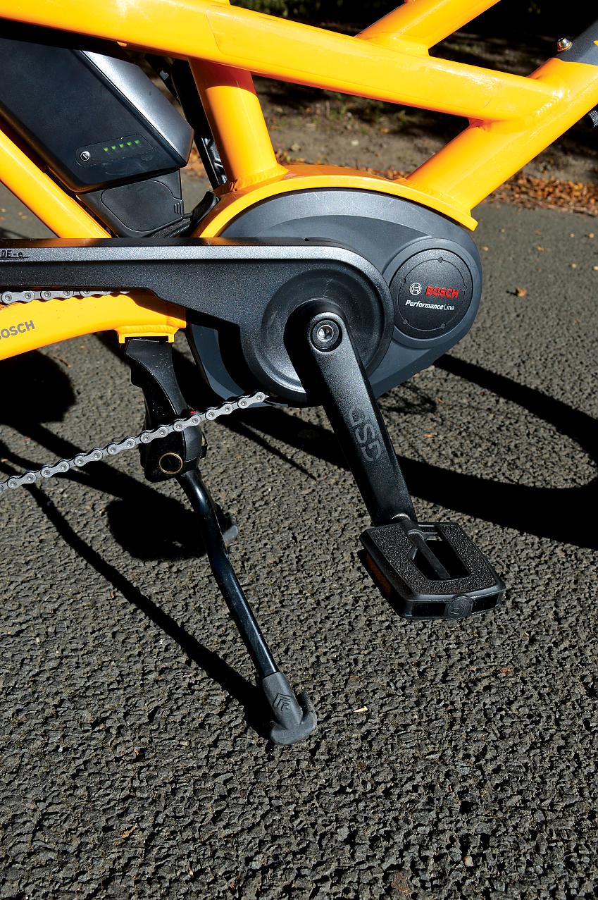 A close-up showing the Tern's pedal, crank, enclosed chainring and chain. The battery can just be seen. The bike is a dark yellow