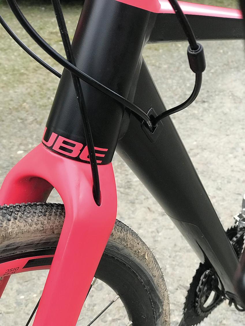 A close-up of the Nuroad's front fork where it meets the head tube and down tube, showing where the cables go into the frame. The tubes are black, the fork bright pink