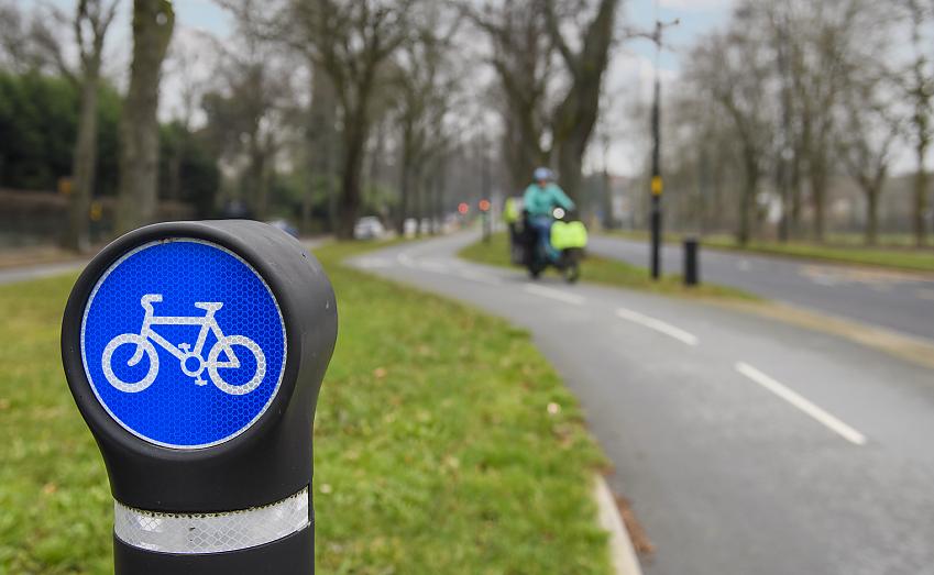 In the foreground, a bollard with a blue cycling traffic sign. In the background, a segregated cycle path.