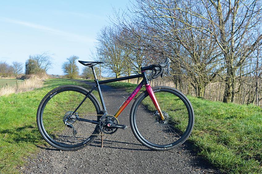 The Isen All Season, a multi-coloured gravel bike propped up on a gravel path