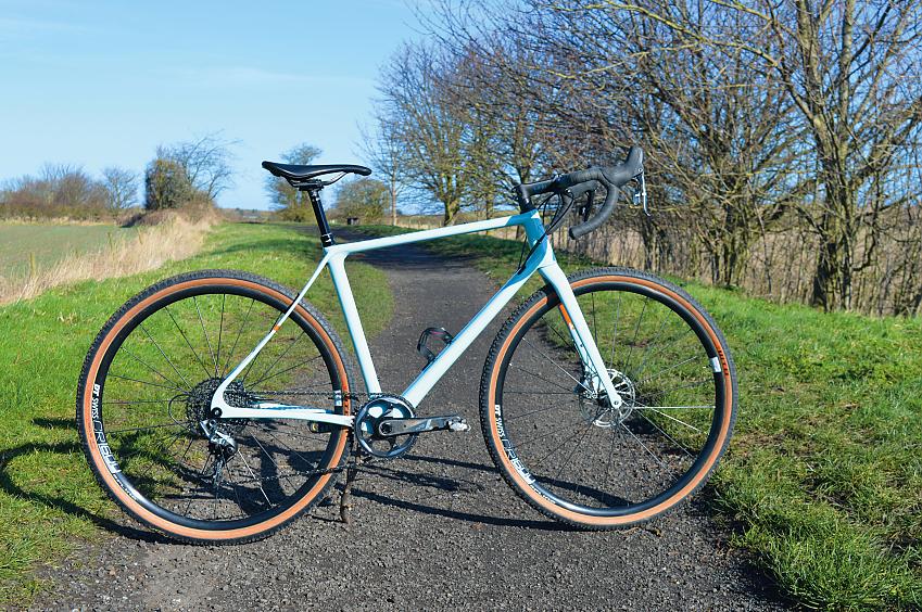The Vielo V+1 UD Force Edition, a very pale blue gravel bike propped up on the same gravel path
