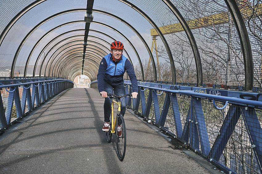 A male cyclist wearing a red helmet rides across a blue bridge