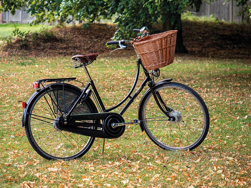 A black roadster bike with wicker basket on the front, rear rack, skirtguard and chainguard. It looks old fashioned and is very pretty