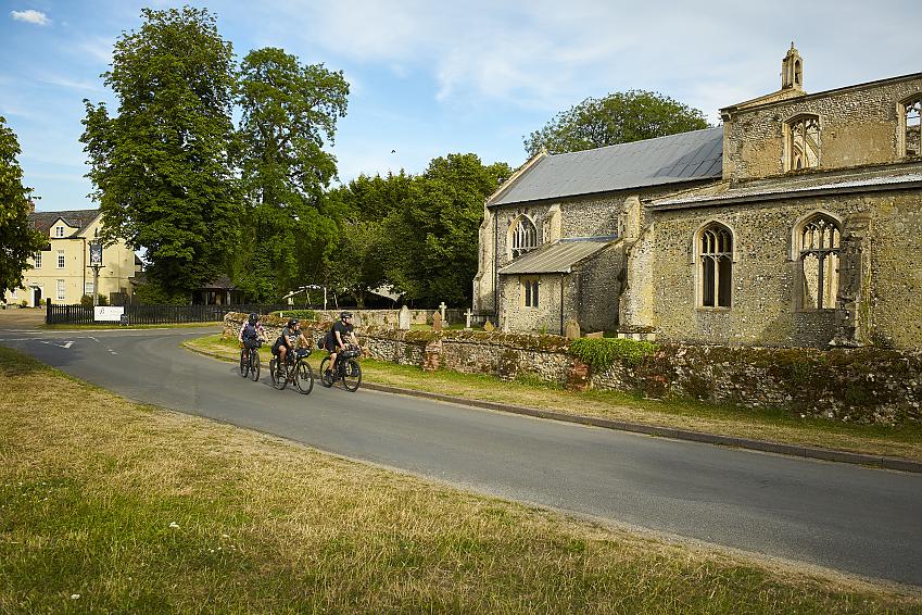 Three cyclists riding past a village church in Norfolk