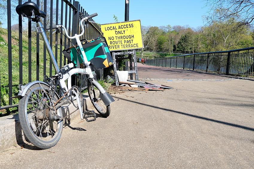 A Brompton folding bike rests up against a fence, in front of a 'Local access only' sign, placed in front of the Lagan Towpath in Belfast