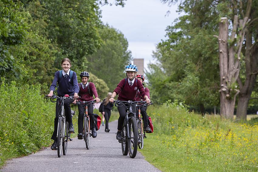 A group of school pupils cycle in school uniform along a greenway