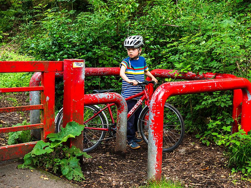 A child with a red bike has had to dismount and walk his cycle through a barrier across a path