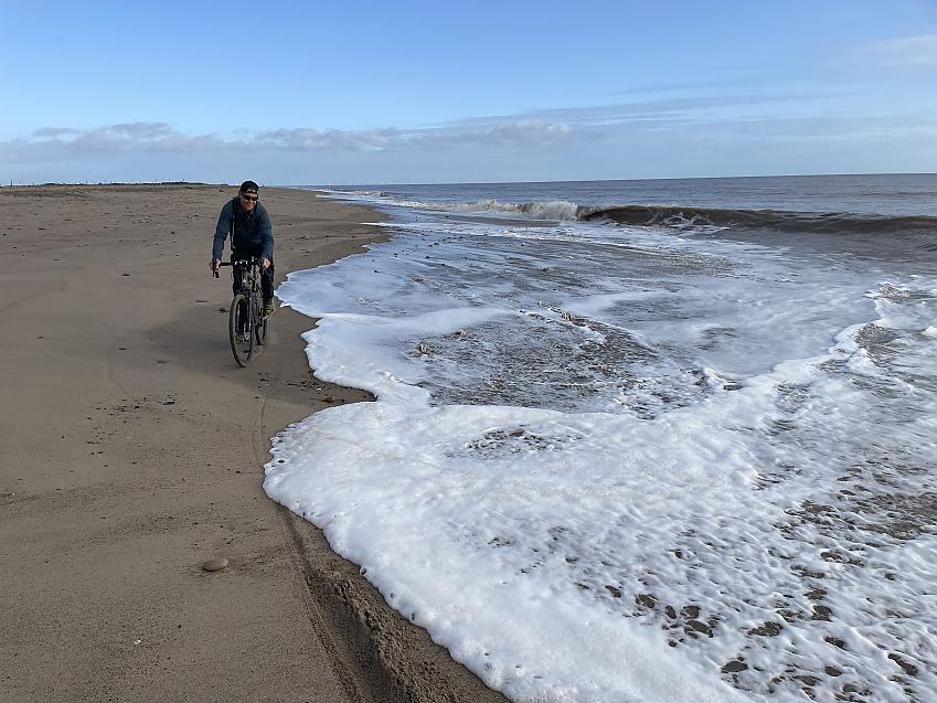 A man is cycling on the beach along the shoreline