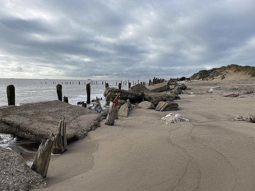 Wooden groynes, concrete blocks and wooden posts stick out of the sand and sea