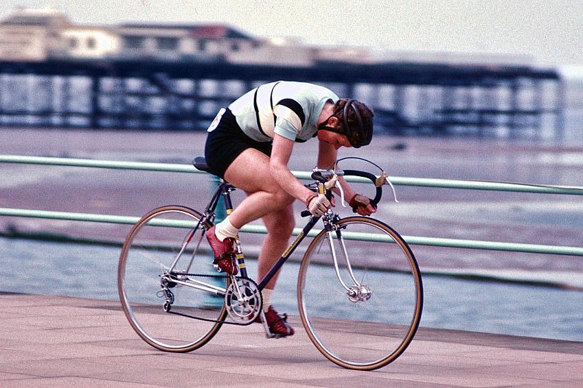 A woman is cycling along the seafront. In the background is a pier. She's on a road bike and is racing