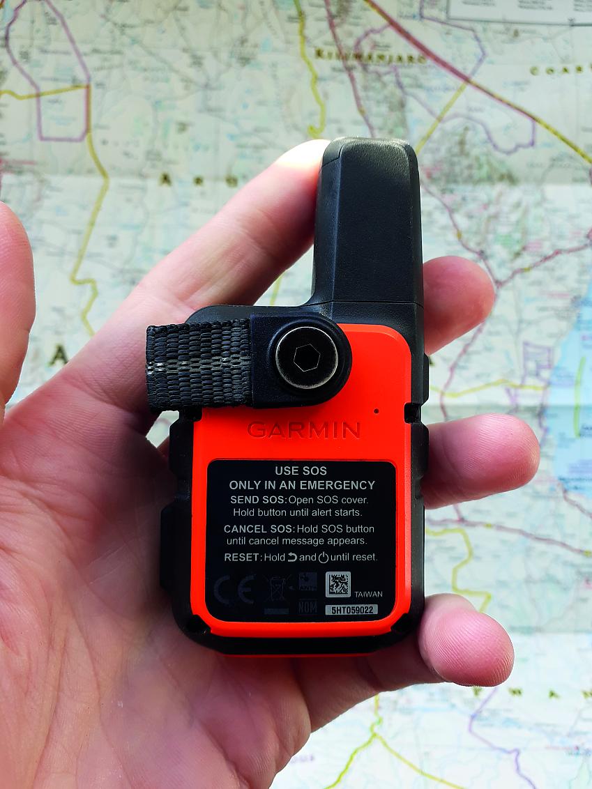 A small handheld GPS unit in orange showing the emergency SOS function. There's a map in the background