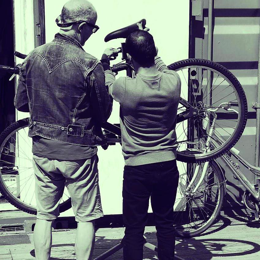Two men are working on a bike that's attached to a workstand