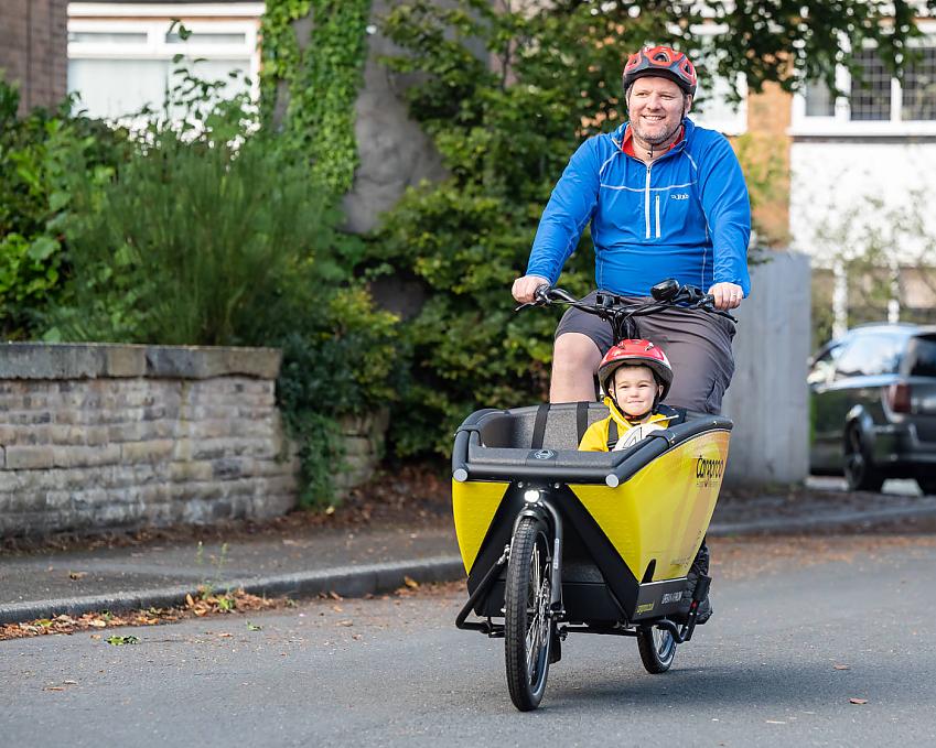 A man carrying a small boy in a hired e-cargo bike in Manchester