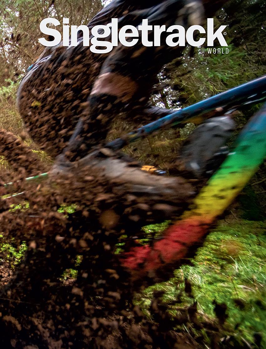 Singletrack World cover, showing a fuzzy close-up of a cyclist's foot as they pedal hard on an off-road track. You can see a bit of a rainbow-coloured bike and lots of mud is flying about