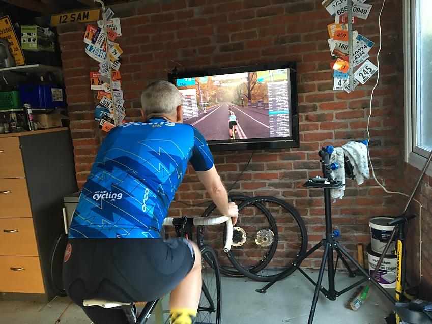 A male cyclist in a Cycling UK jersey using a turbo trainer in a garage
