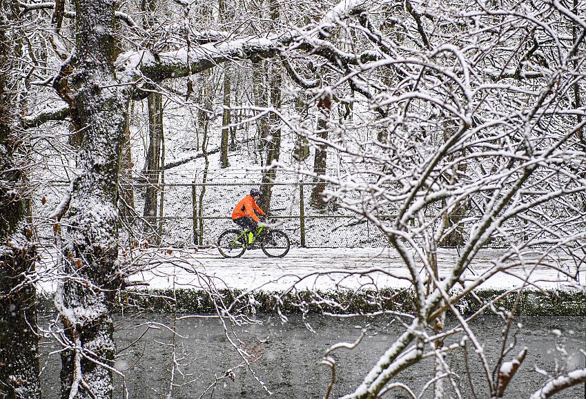 A cyclist is cycling along a tow path in the snow. It's a very wintry scene and the cyclist is wearing a bright orange waterproof jacket.