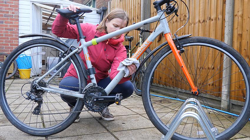 A person is cleaning a grey and orange hybrid bike using a cloth