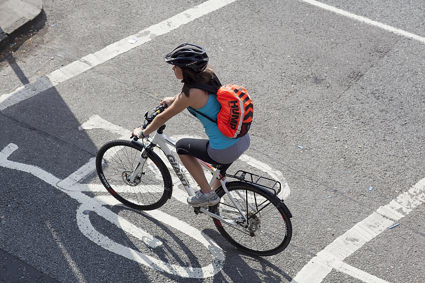 A woman on a white hybrid bike is stopped in an advanced stop line. She is wearing sporty clothing and has a rucksack on her back